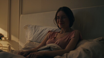Smiling girl resting bed before sleep. Joyful happy woman dreaming at cozy home.