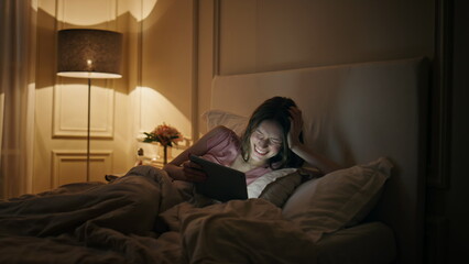 Obraz premium Girl watching funny tablet video movie at night. Happy woman resting home bed
