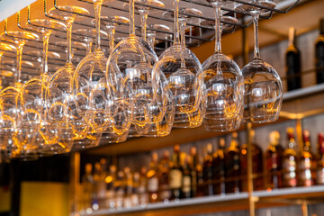 A group of wine glasses hanging upside down on a bar rack, bottles of liquor in the background