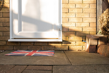 Abstract view of a garage side door seen in bright window sunlight. An ornate, flag  door mat is seen outside.