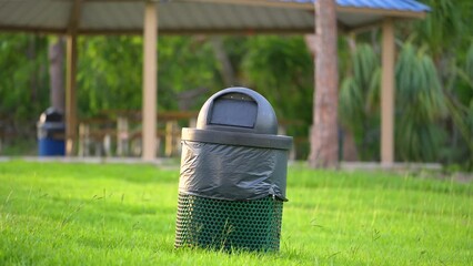Green recycling bin with plastic bag on green lawn in town park. Litter collection concept