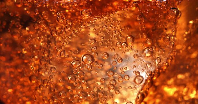 Super slow motion macro of old campari spritz cocktail with ice cubes in transparent glass is being mixed by bartender in bar or club.