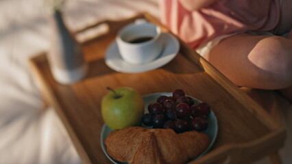 Closeup hotel bed breakfast on tray. Unknown woman body rest in golden sunlight