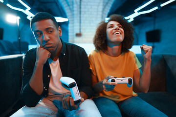 A player sulks while their opponent celebrates a victory in a vibrant gaming den.