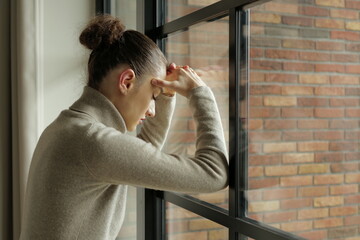 Portrait of a sad upset young  woman thinking standing by the window