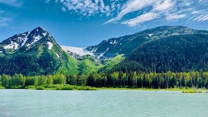 Eternal snow on Girdwood Glacier in Alaska USA under clear blue Sky and in front a grey blue lake - landscape shot taken on the water from a boat: concept of summertime, travel, outdoor