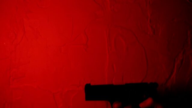 Cinematic red color. Silhouette of hand holding gun. Closeup unknown arm in spotlight background. Unrecognizable person in dark. Studio, 4K, walther 88