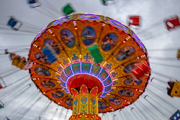 Um brinquedo gigante de rotação no parque de diversões com poucas pessoas, em um dia nublado. Foto feita de baixo para cima. - obrazy, fototapety, plakaty