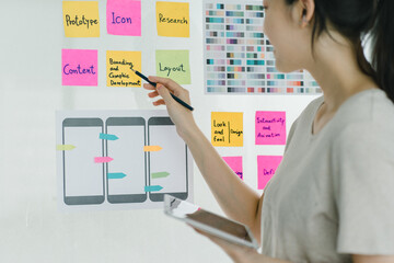 Young asian designer brainstorming app interface with colorful sticky notes.