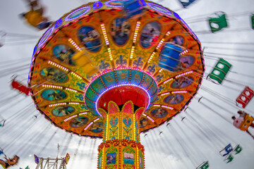 Um brinquedo grande e colorido no parque de diversões com poucas pessoas, em um dia nublado. Foto feita de baixo para cima. - obrazy, fototapety, plakaty