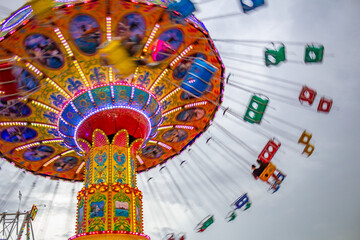 Detalhe de um brinquedo gigante de rotação no parque de diversões com poucas pessoas, em um dia nublado. Foto feita de baixo para cima.