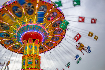 Um brinquedo gigante de rotação no parque de diversões com 2 pessoas em um dos balanços, em um dia nublado. Foto feita de baixo para cima. Imagem feita com baixa velocidade da câmera.