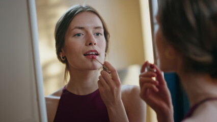 Woman applying shiny lipstick in mirror reflection closeup. Attractive girl do