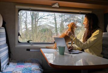 Woman petting her dog while working on computer while traveling in motorhome
