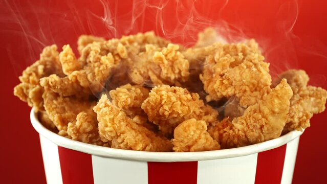Slow Motion of Rotating Fried Chicken Pieces in Bucket on Colored Background. Fresh Crispy Chicken with smoke, Rotating on Turntable.