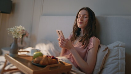 Home girl using smartphone in cozy bedroom closeup. Relaxed smiling woman look