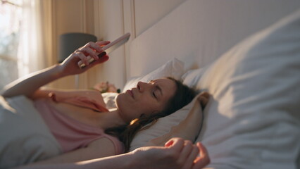 Woman turning off alarm clock in early morning. Unhappy girl going back to sleep