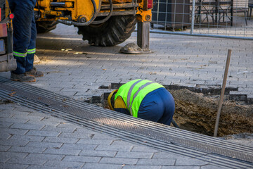 Maintenance workers on site repairing damaged water pipe under the street pavement - obrazy, fototapety, plakaty