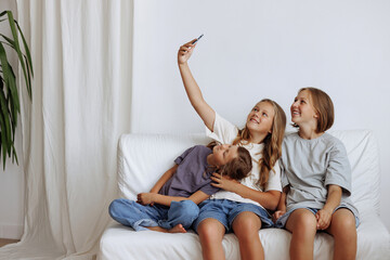 Three girls take a selfie while sitting on the sofa. Three sisters smiling in casual clothes...