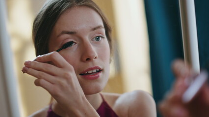 Smiling model applying mascara on eyelashes closeup. Attractive girl admiring