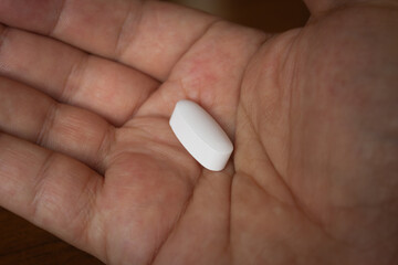 Close-up of an adult hand holding a single white pill, healthcare concept