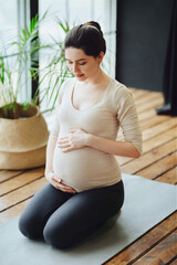 Meditation during pregnancy. Young calm tranquil pregnant woman doing yoga at home, meditating and practicing mindfulness, expectant mother sitting in lotus pose with closed eyes