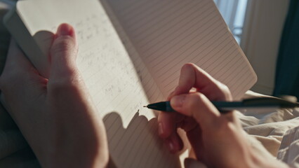 Female hands writing diary in sunlight closeup. Woman making notes in morning