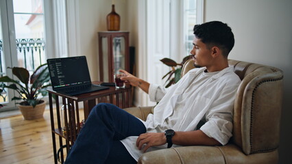 Relaxed man drinking cola at armchair. Serious guy checking smartphone at home