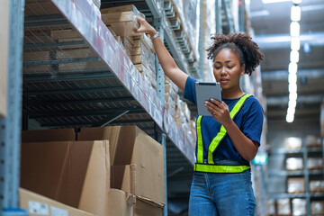 Black African American woman holding a tablet sits checking inventory and checking orders from...