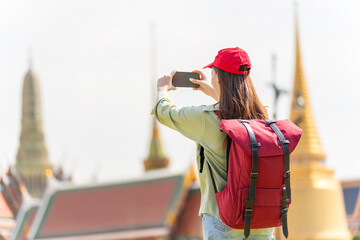 Young asian woman traveler with phone capturing moments and exploring Wat Phra Kaew and The Grand Palace in a happy and casual style during a sunny day