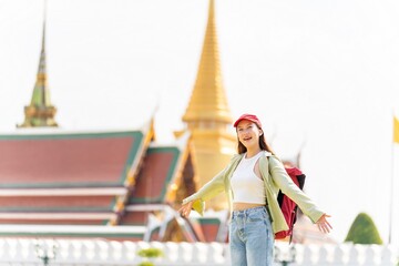Young asian woman backpacker traveler exploring Wat Phra Kaew and The Grand Palace in a happy and casual style during a sunny day