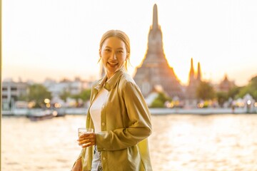 Young Asian Woman Traveler Holding a Drink While Enjoying The Sunset Moments of Wat Arun by the...