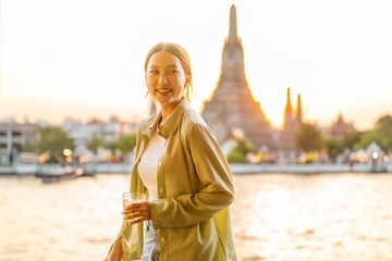 Young Asian Woman Traveler Holding a Drink While Enjoying The Sunset Moments of Wat Arun by the...
