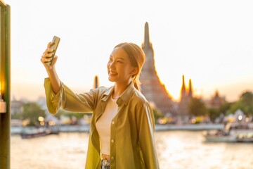 Young Asian Woman Traveler Taking a Selfie While Enjoying The Sunset Moments of Wat Arun by the...