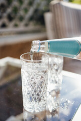 Pouring sparkling water from the bottle into glass. Water drink pouring into glass, garden background.