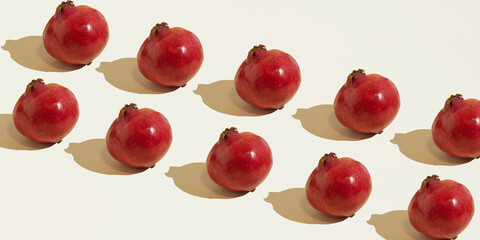 Isolated pomegranate fruits laid out diagonally in two rows against a beige background. Copy space, minimal food concept. Healthy nutrition.