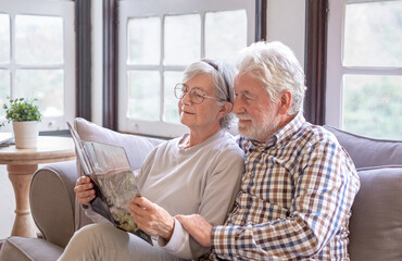 Serene white-haired senior couple sitting on the sofa in the living room reading travel information...
