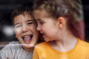 Cute kids are sitting on floor outside panoramic window. Happy boy and girl sincerely smile each other.
