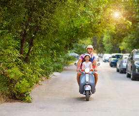 Happy young father and little daughter riding a vintage scooter in the street wearing hats