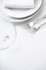 Place setting. Clean, minimal, white plates, white tablecloth, stainless forks, shallow depth of field. 