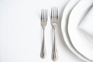 Place setting. Clean, minimal, white plates, white tablecloth, stainless forks, shallow depth of field. 