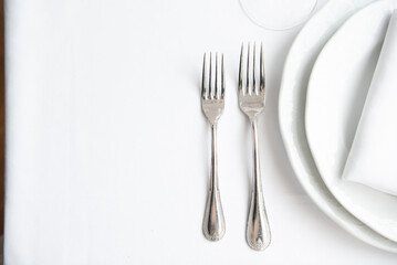 Place setting. Clean, minimal, white plates, white tablecloth, stainless forks, shallow depth of field. 