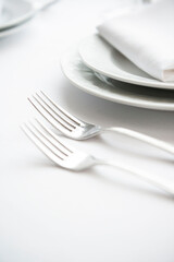 Place setting. Clean, minimal, white plates, white tablecloth, stainless forks, shallow depth of field. 