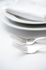 Place setting. Clean, minimal, white plates, white tablecloth, stainless forks, shallow depth of field. 