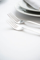 Place setting. Clean, minimal, white plates, white tablecloth, stainless forks, shallow depth of field. 