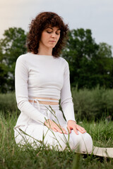 Concept of calmness. Sports woman sitting on yoga mat put hut on her lap. Female focused on...