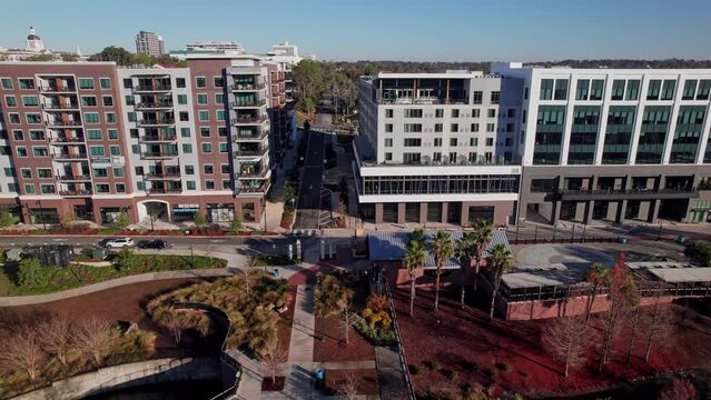 Florida new high-rise building full of mixed use apartments, businesses, event venues, and sidewalks by outdoor park from drone shot and aerial view with motion