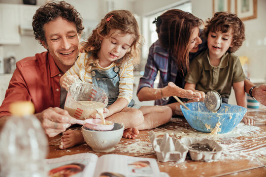 Family baking together in the kitchen with children making a mess