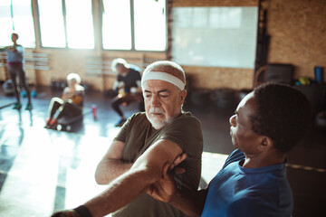 Senior man being assisted by a personal trainer during a stretching exercise in a gym