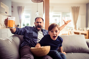 Excited father and son cheering while watching sports on TV at home